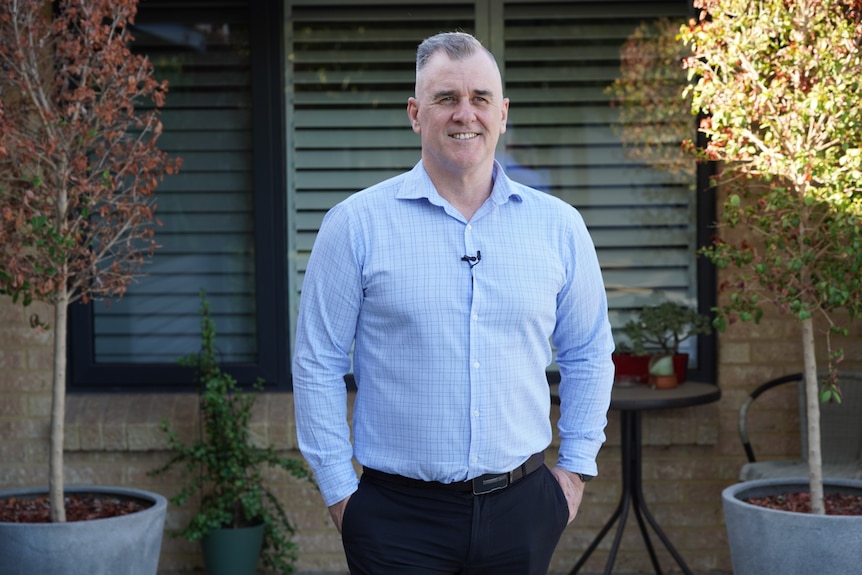 A man stands smiling outside a home. 