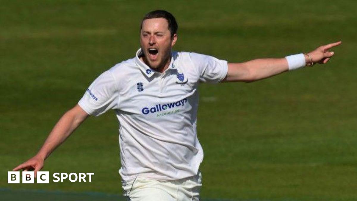 Sussex bowler Ollie Robinson celebrates a wicket with both arms out wide pointing, shouting, wearing club whites and sussex crest, with white wrist band on left wrist partially coveri ng siver bracelet