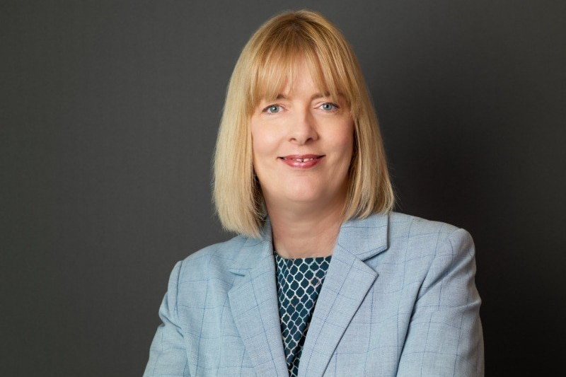 A woman with cropped blonde hair, wearing a blue blazer and smiling.
