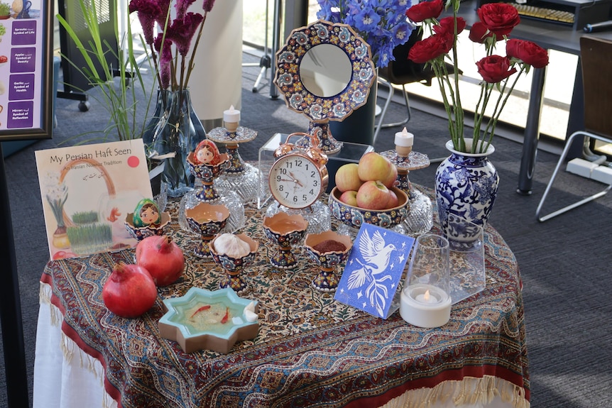 Haft seen items on table including apples, pomegranates and flowers. 