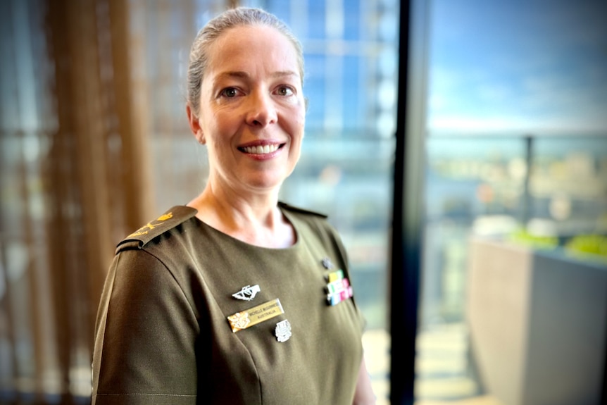 Smiling Michelle in khaki uniform, hair slicked back, has medals and rank pinned on both sides.