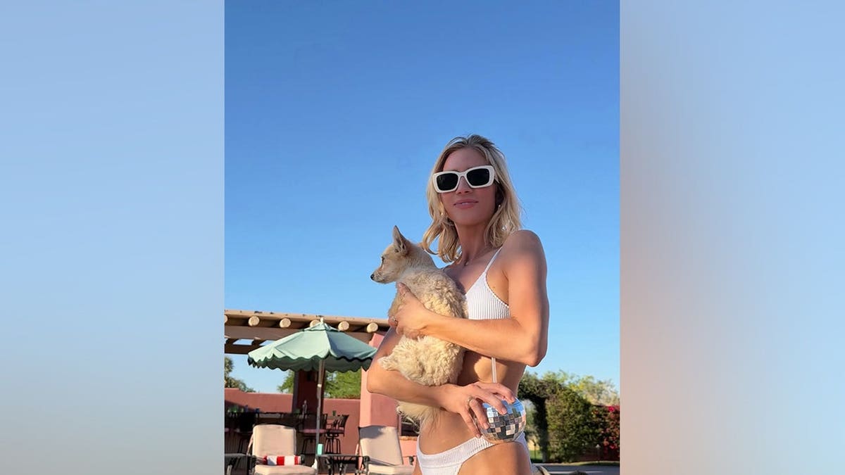 Brittany Snow posing in a white ribbed bikini and mod sunglasses while holding a small dog and a disco ball cup.