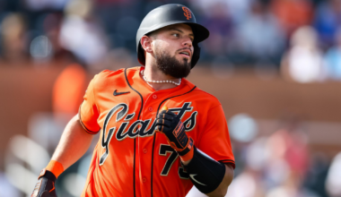 A baseball player in a bright orange San Francisco Giants uniform runs, wearing a black helmet, batting gloves, and a pearl necklace.