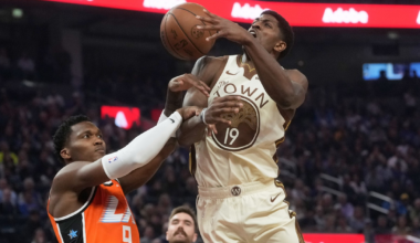 A basketball player in a white "The Town" jersey leaps for a shot as a defender in an orange jersey attempts to block him mid-air.