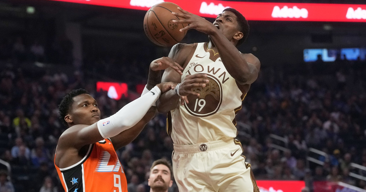 A basketball player in a white "The Town" jersey leaps for a shot as a defender in an orange jersey attempts to block him mid-air.