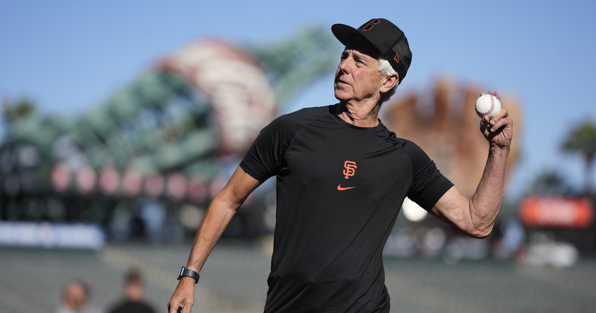 A man in a black San Francisco Giants shirt and cap prepares to throw a baseball on a sunny day at a stadium.