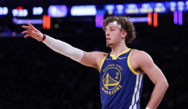 A Golden State Warriors player with curly hair points with his left arm extended, wearing a blue jersey numbered 2 and a white arm sleeve.