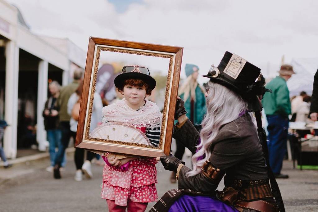 child and adult dressed as characters, with the child holding a frame around their face, on the main street at Clunes Booktown Festival