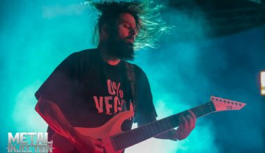Stephen Carpenter playing guitar on stage during a live Deftones concert, with dramatic stage lighting and audience in the background.