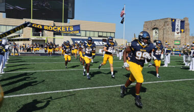 Toledo football players run onto the Glass Bowl field as the band plays next to them.