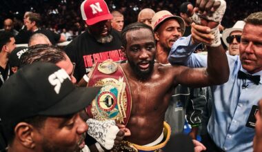 Terence Crawford holding championship belts in the ring surrounded by his team after a fight
