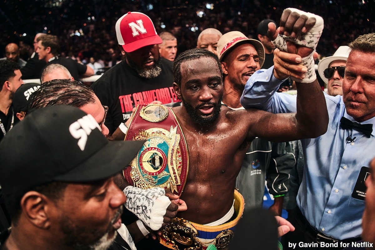 Terence Crawford holding championship belts in the ring surrounded by his team after a fight