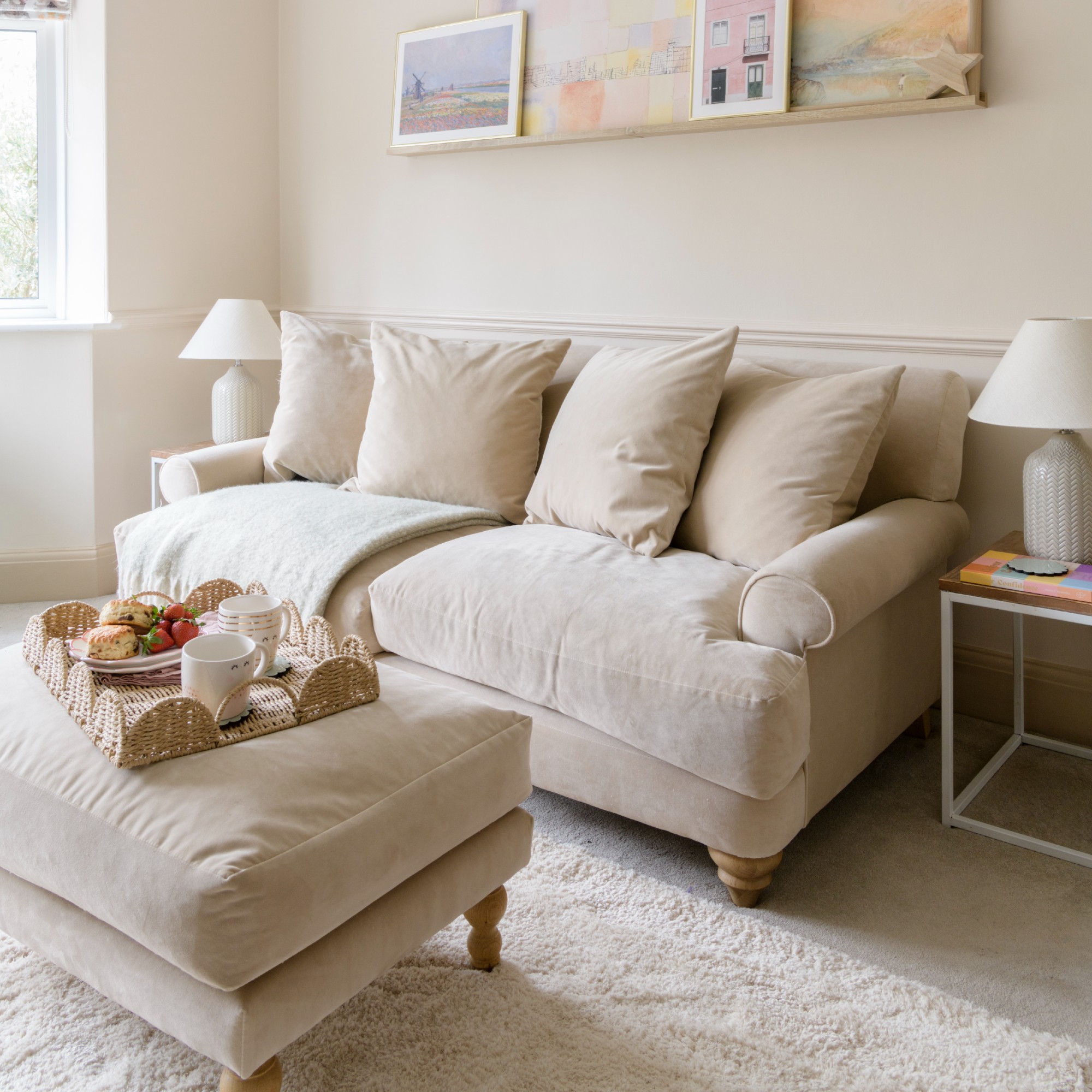 A tonal beige living room with a velvet sofa with tapered legs and a matching ottoman