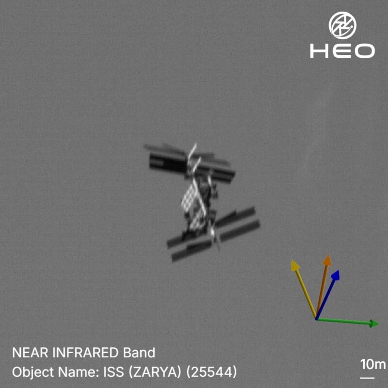 Infrared image of the International Space Station (ISS) showing its structure against a gray background, with HEO logo at the top right and a scale indicating 10 meters at the bottom right.