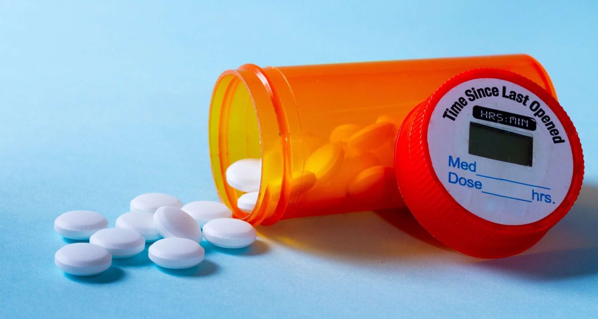 White pills falling out of prescription bottle on blue background
