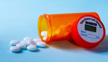 White pills falling out of prescription bottle on blue background