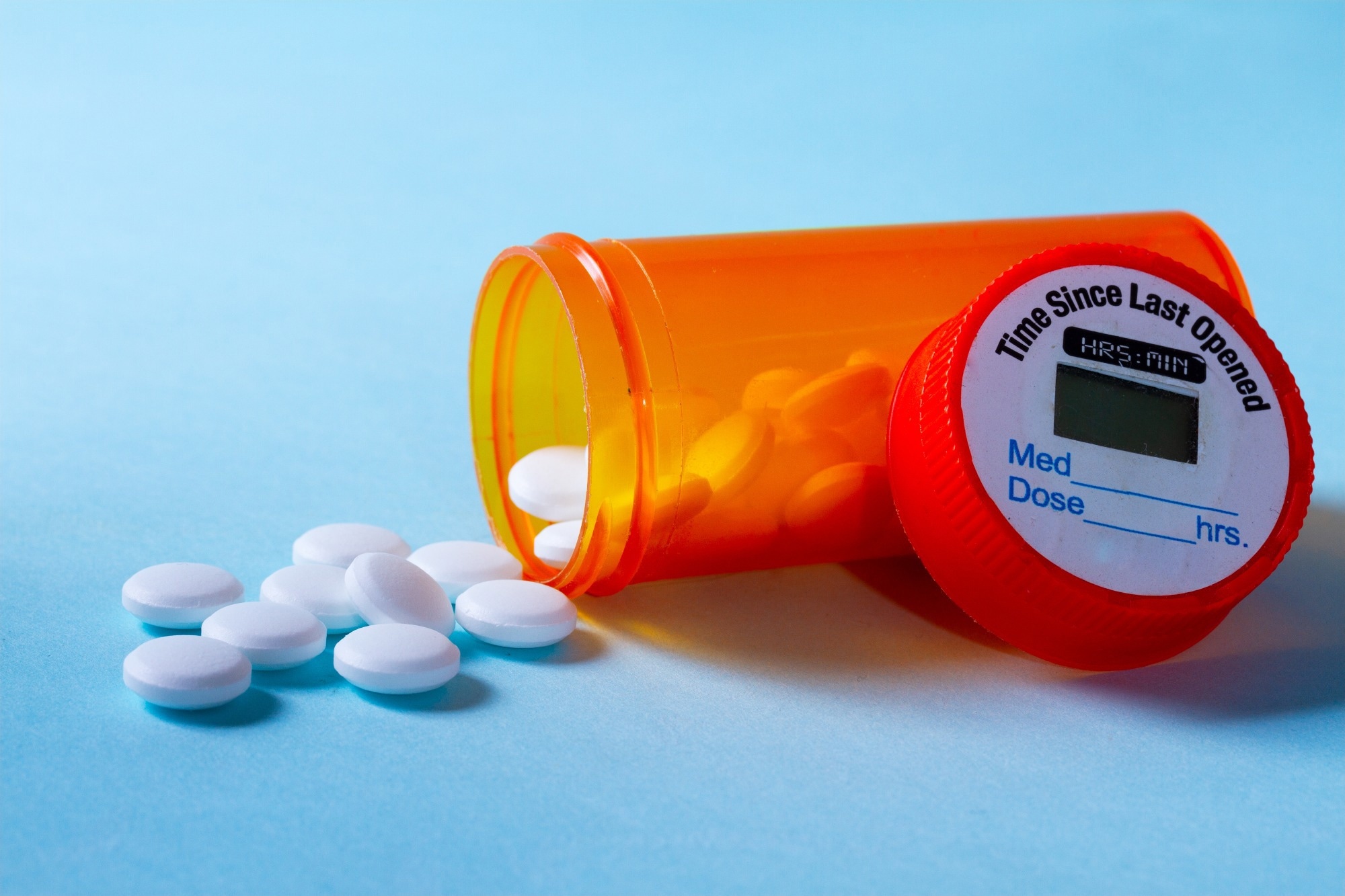 White pills falling out of prescription bottle on blue background