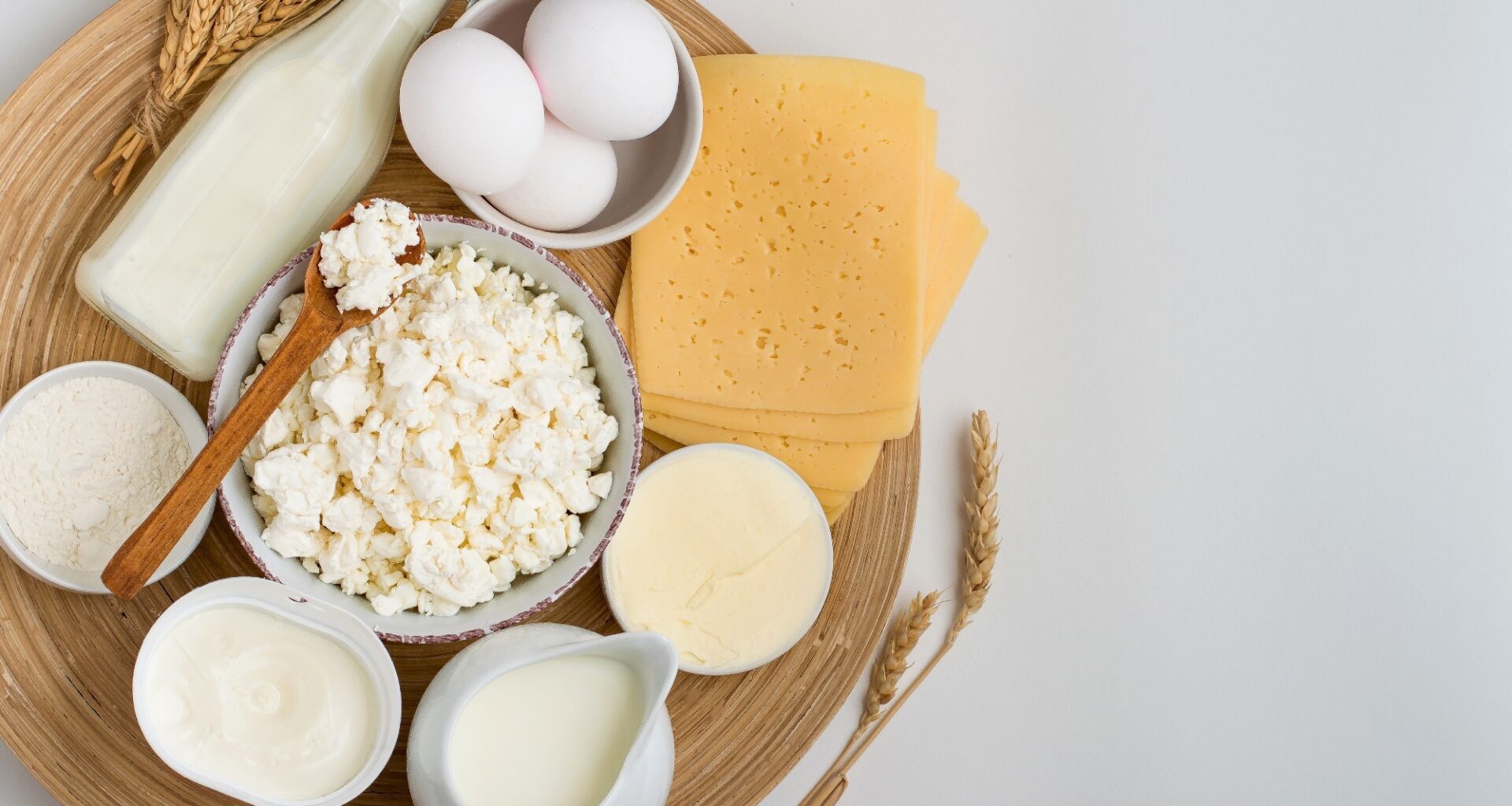 Assortment of dairy products, milk, cottage cheese, cheese, cream cheese, butter, eggs and yogurt on a wooden stand on a light background.