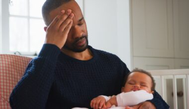Stressed New Father Sitting In Chair Holding Sleeping Baby Girl In Nursery At Home