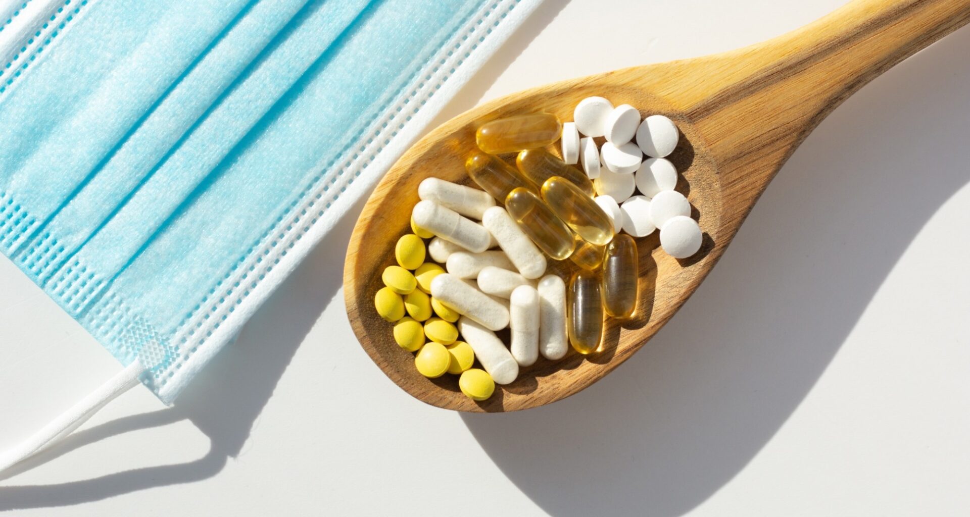 Closeup of probiotic tablets on wooden spoon next to face masks. Concept of supplementation during the pandemic.