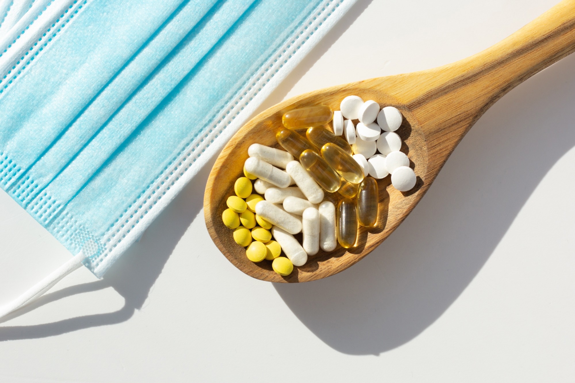 Closeup of probiotic tablets on wooden spoon next to face masks. Concept of supplementation during the pandemic.