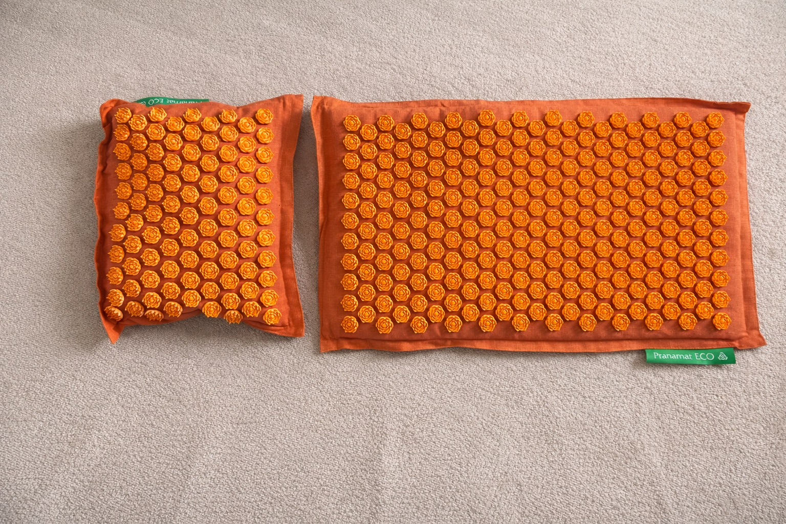 An orange mat and pillow with lots of small lotus-shaped spikes laying on a carpet