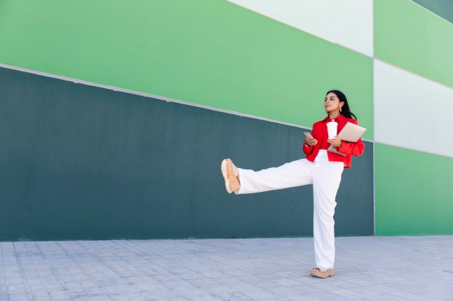 Businesswoman using smartphone while holding laptop outdoors