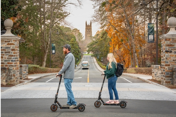 Couple on scooters with Duke Chapel in background.