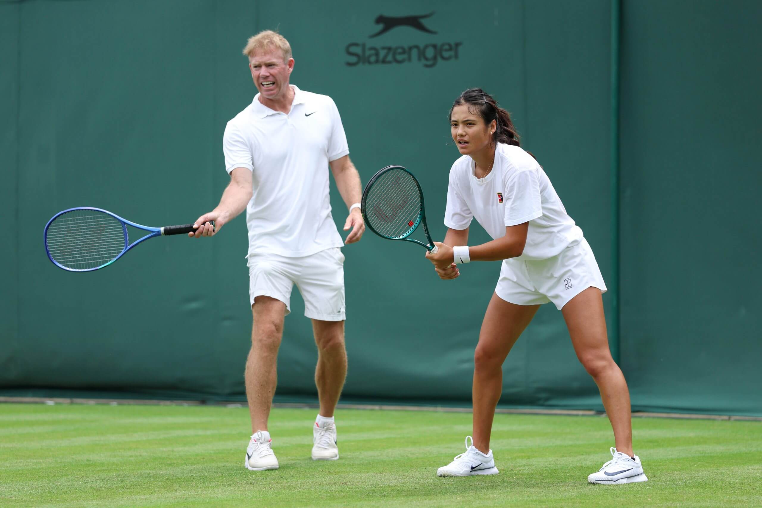 Mark Petchey (left) demonstrates a forehand grip while Emma Raducanu (right) stands in her return position, on a grass tennis court.