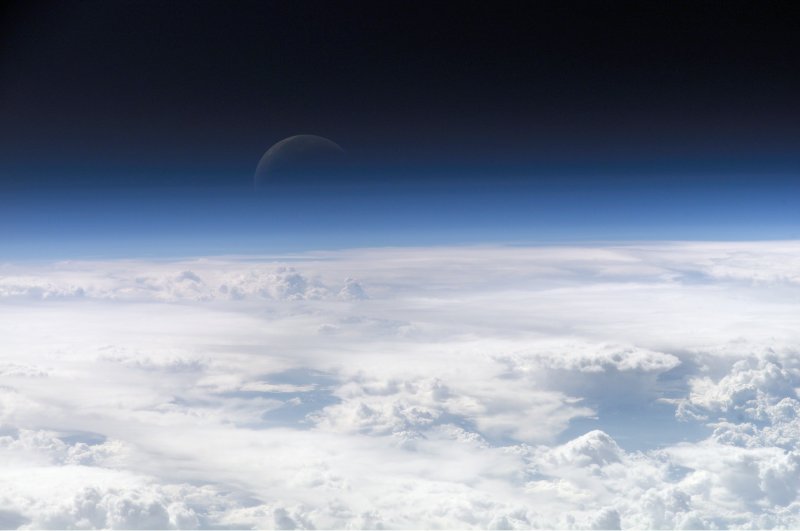 Top of Earth's atmosphere, with cloud cover and Moon vaguely visible. (Credit: NASA)