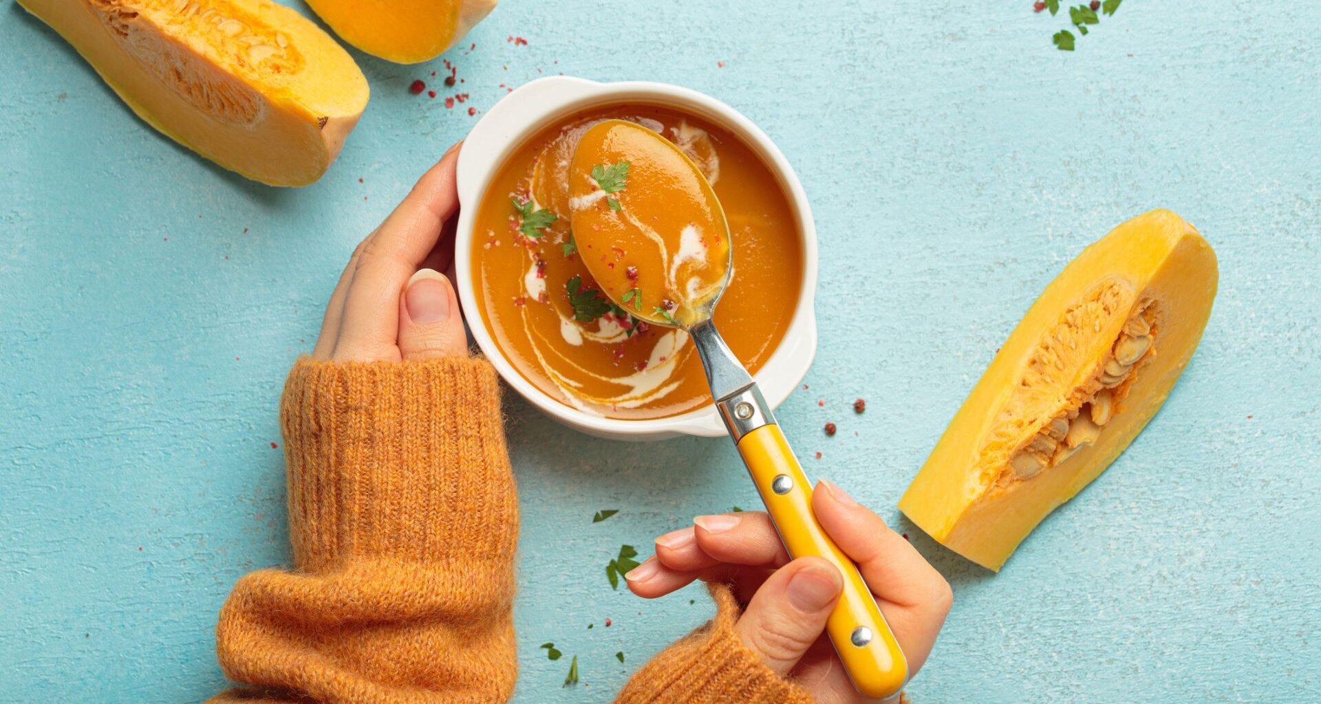 a woman's hands holding a bowl of squash soup with butternut squash slices scattered on the table
