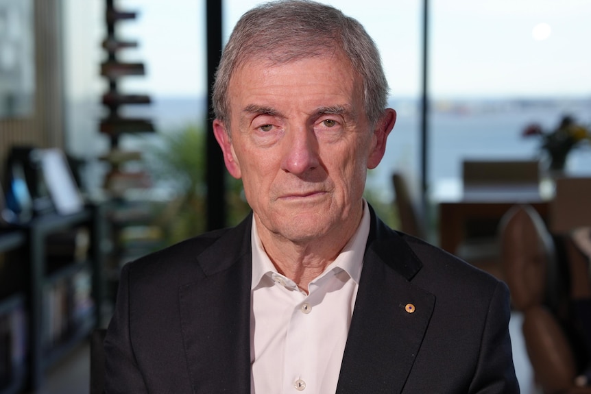 A grey-haired man in a suit with no tie fills the frame