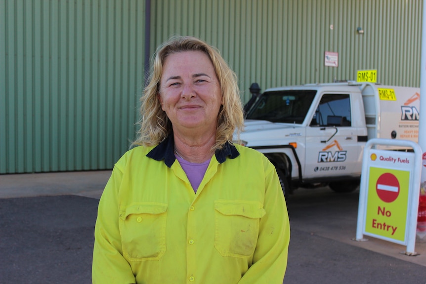 A woman with blond hair and wearing high visibility clothing smiles.