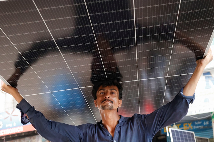 A worker carries a solar panel sheet on his head
