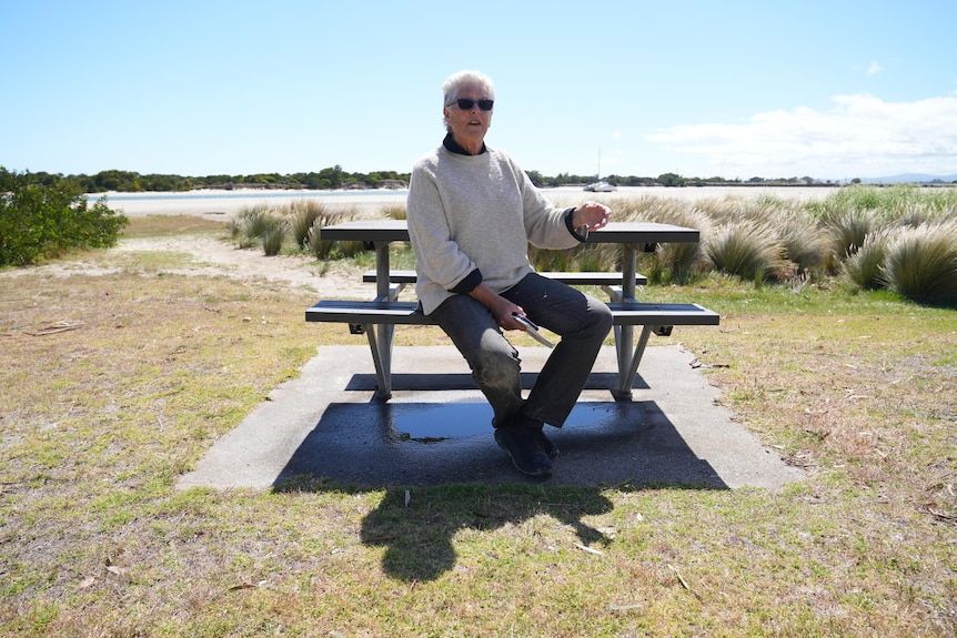 She sits at a picnic table with the Bridport channel behind. 