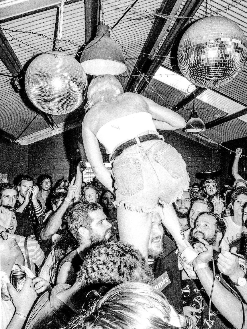 Black and white photo of a chaotic music event with woman climbing over lively crowd