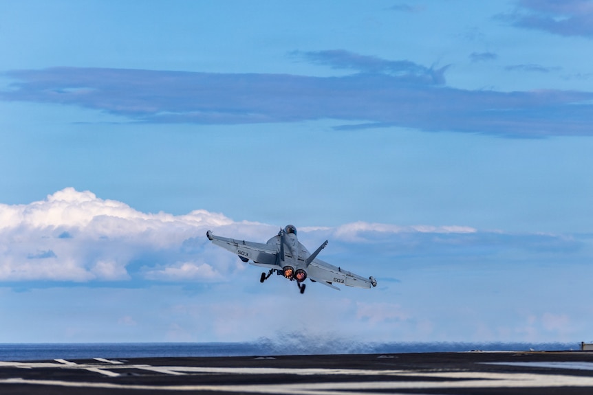 A fighter jet takes off from the deck of an aircraft carrier.