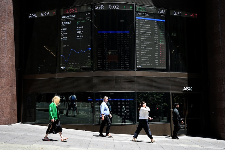 People walk past the front of a large building.