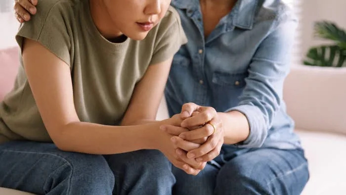 Two people sitting closely, one appears to be comforting the other by holding their hands