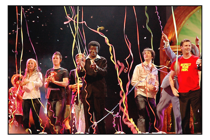 Six people stand on stage while streamers fall from the ceiling.