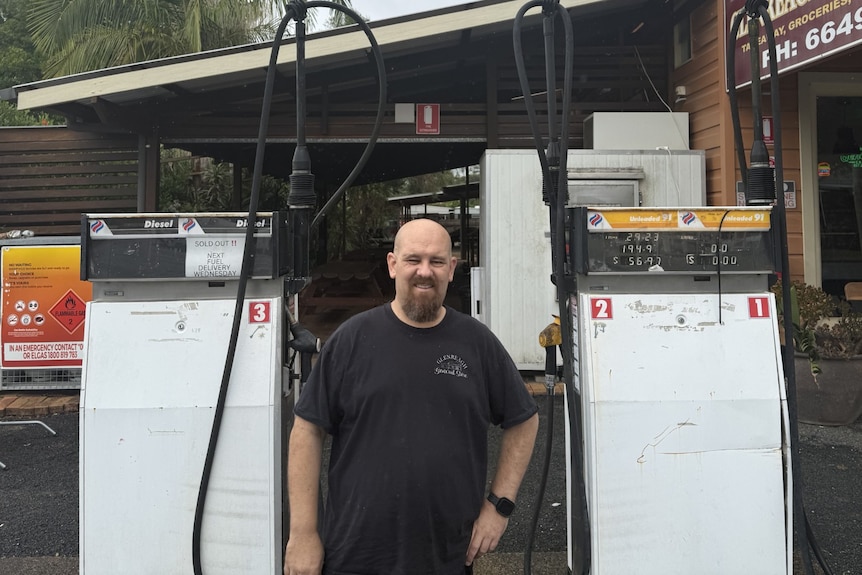 A man stands in front of two fuel bowsers, one of them is empty.