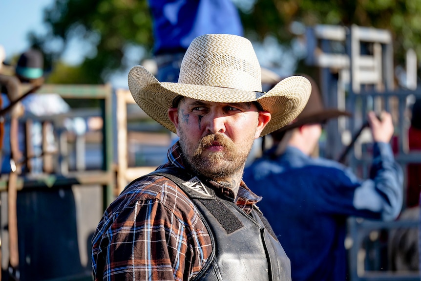 A cowboy with tattoos on his face looking away
