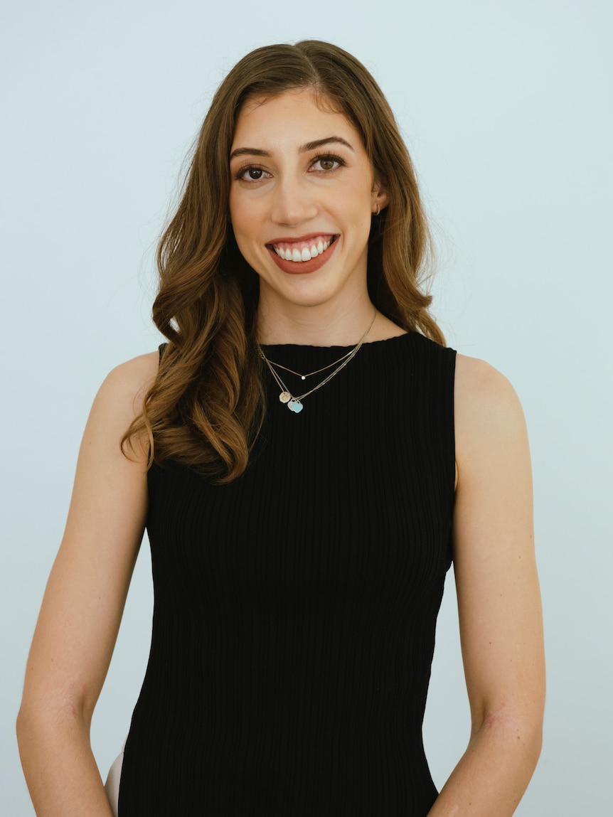 A women with dark hair smiles, weaking a black top. 