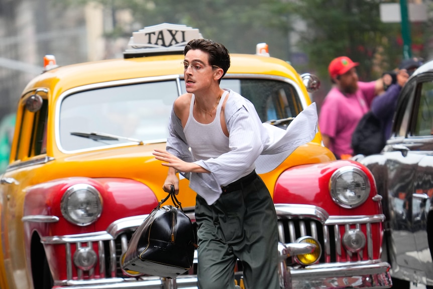 A man carrying a bag runs in front of a taxi cab