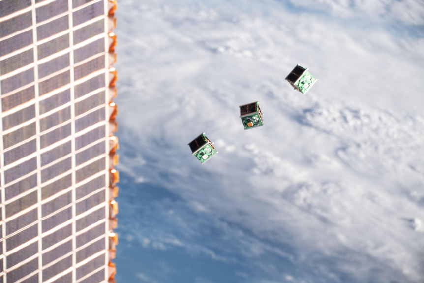 Three small cube-shaped satellites moving away from a launch vehicle in space.