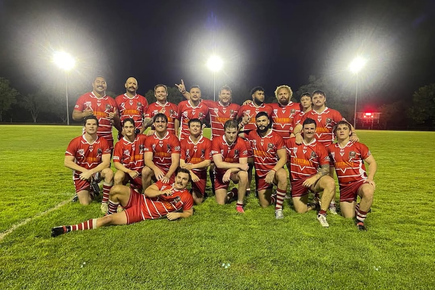 Men wearing a red jersey posing for a camera with lights in the background. 