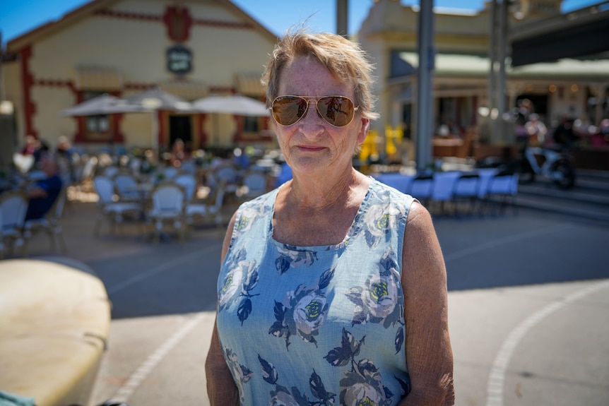 A woman with sunglasses in front of dining tables and umbrellas outside a restaurant