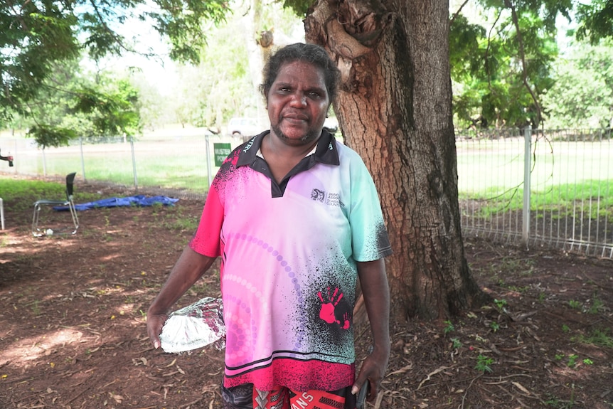 An indigenous woman in a standing in a park in front of tree.
