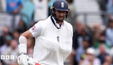 Chris Woakes grimaces with one arm in a sling and his bat in the other