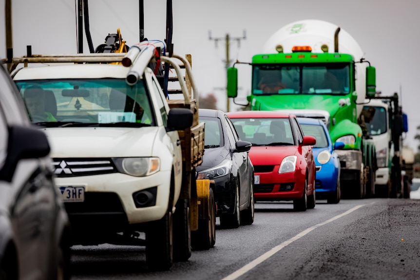Cars queue on a road under overcast skies.